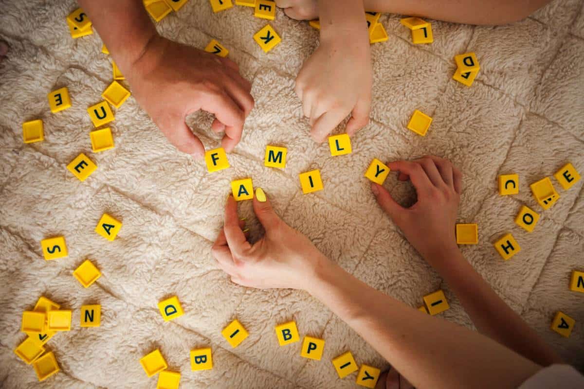Several individuals engaged in a playful activity with large letters scattered on a rug, creating a lively atmosphere.