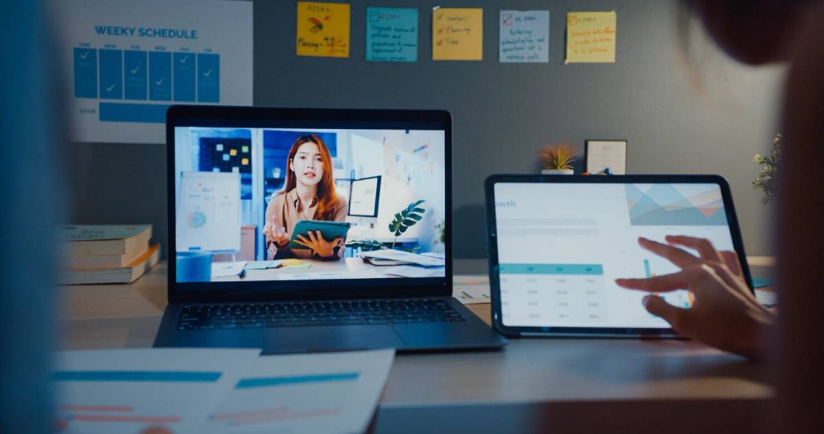 A woman engaged in a video call using both a laptop and a tablet, focused on her conversation.