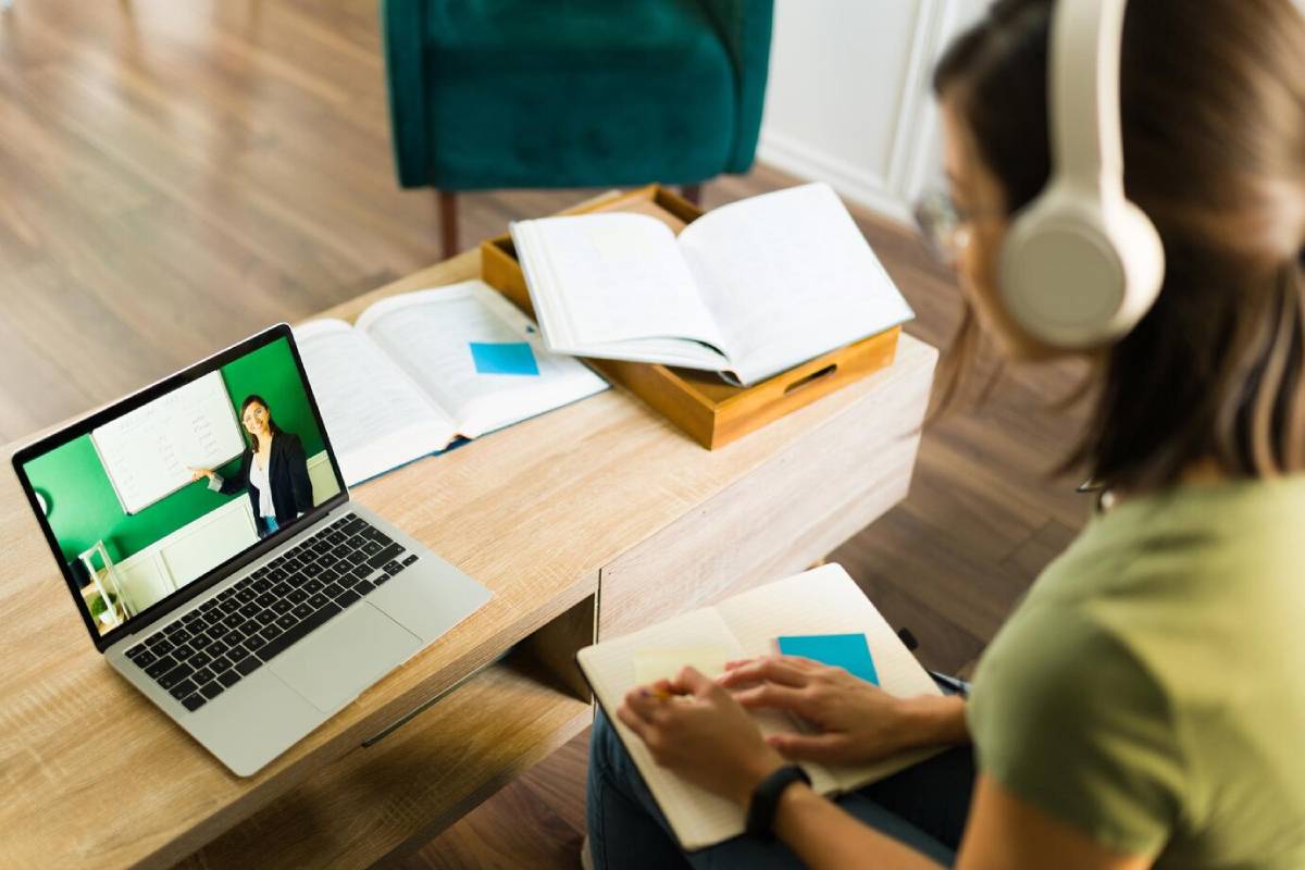 A woman wearing headphones sits at a desk, focused on her laptop while working or attending a virtual meeting.