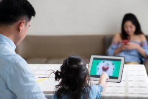 A man and a young girl sit at a table, engaged with a tablet, sharing a moment of learning or play.