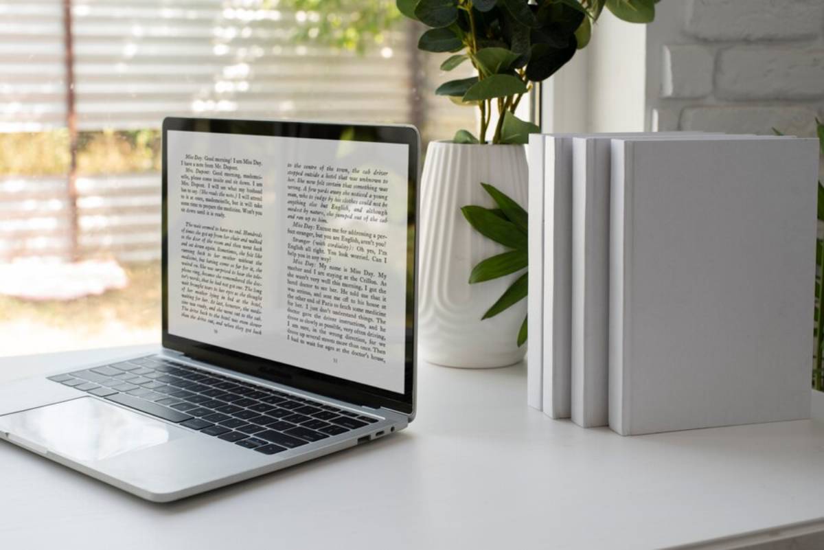 A laptop sits on a desk surrounded by books and potted plants, creating a cozy workspace atmosphere. 