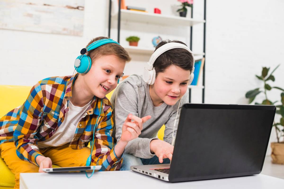Two boys wearing headphones are focused on a laptop screen, engaged in an activity together. 