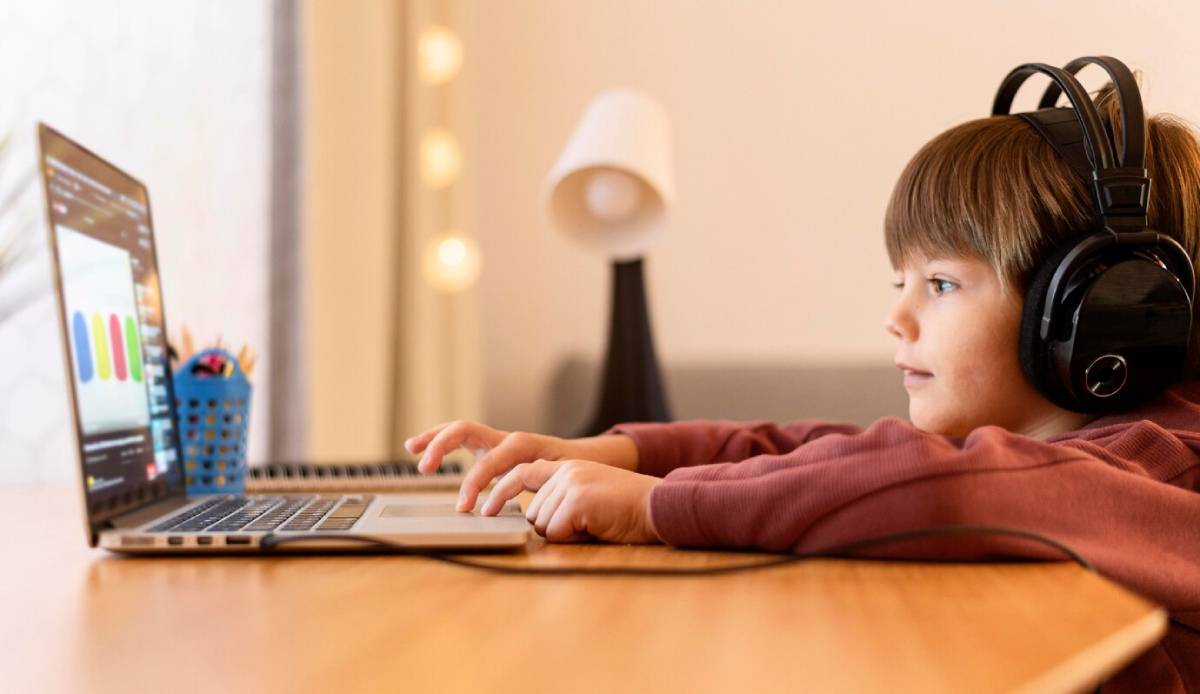 A young boy with headphones is focused on using a laptop, engaged in an activity or task.