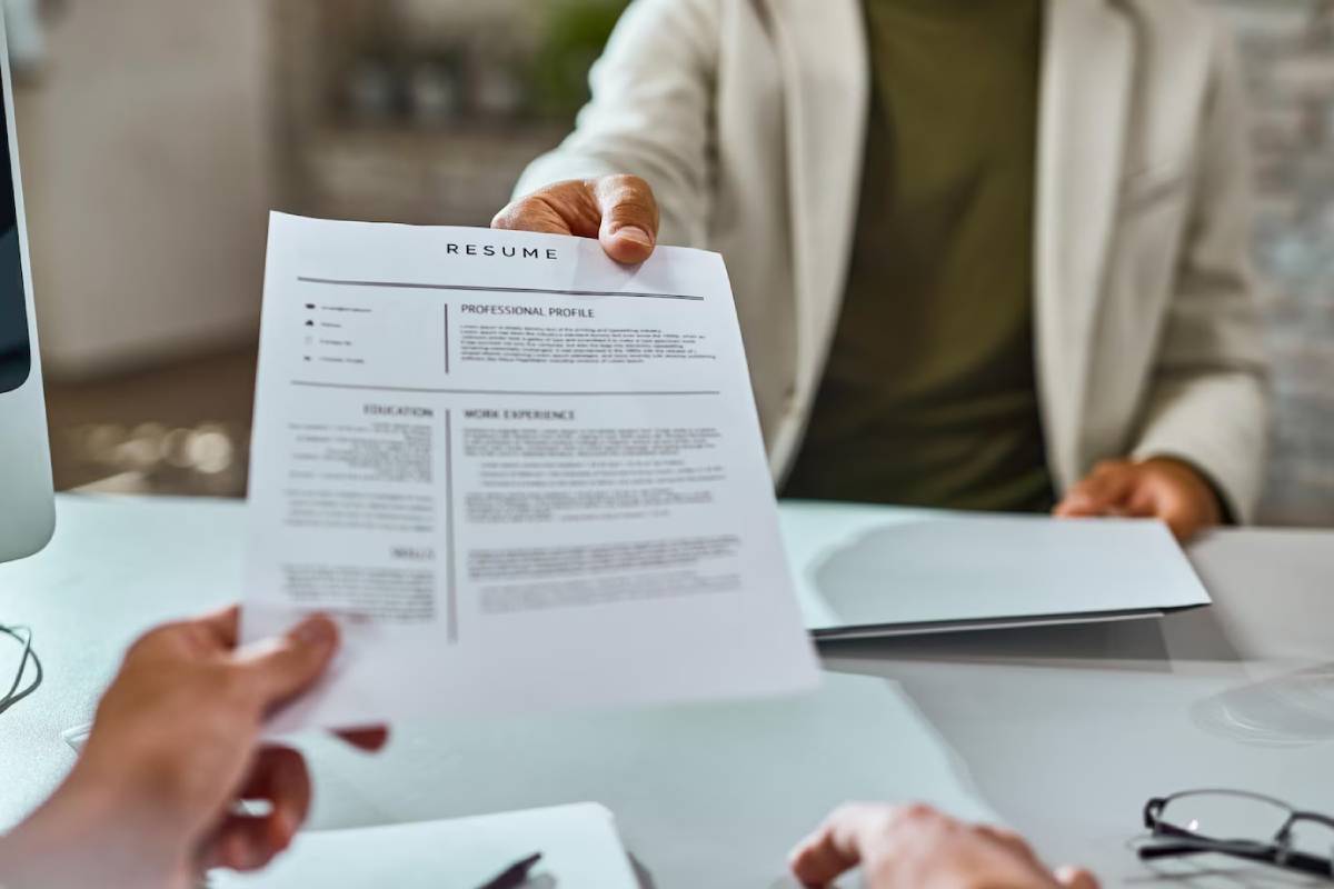 A person holds a resume in front of a computer, preparing for a job application or interview.
