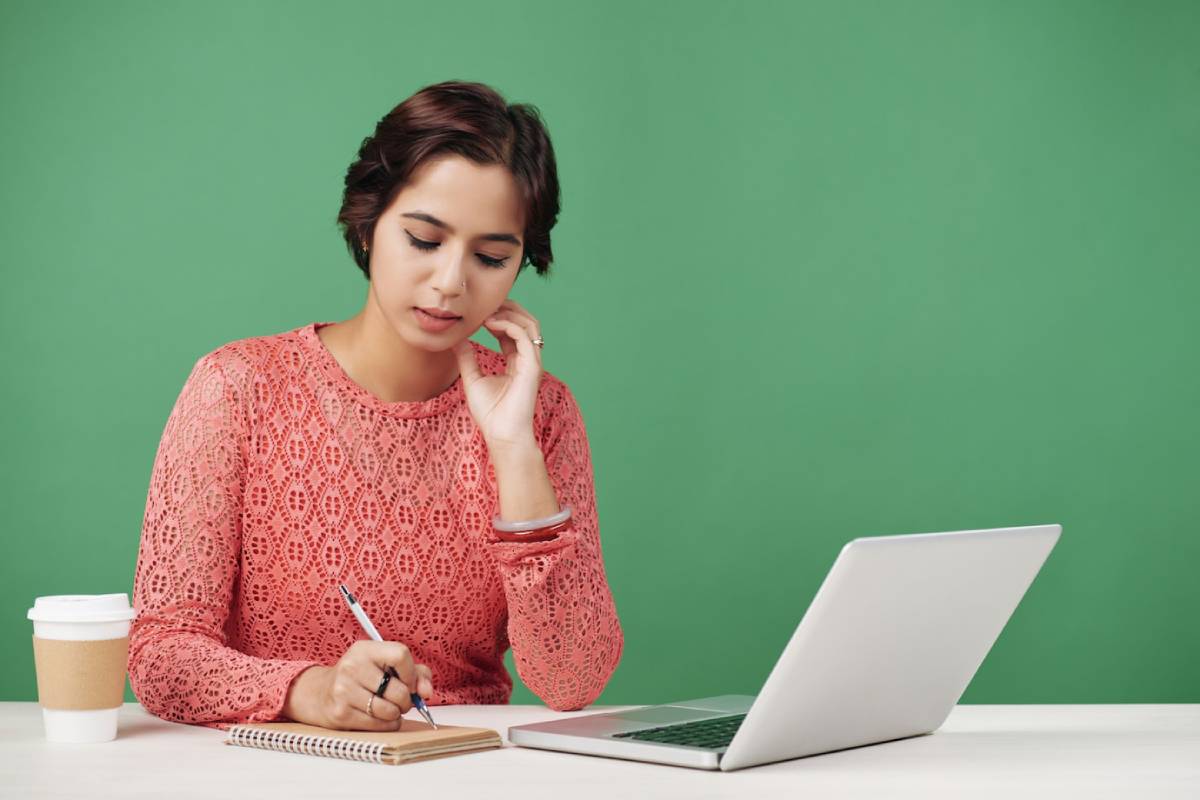 A woman sits at a desk with a laptop open and a cup of coffee beside her, focused on her work.