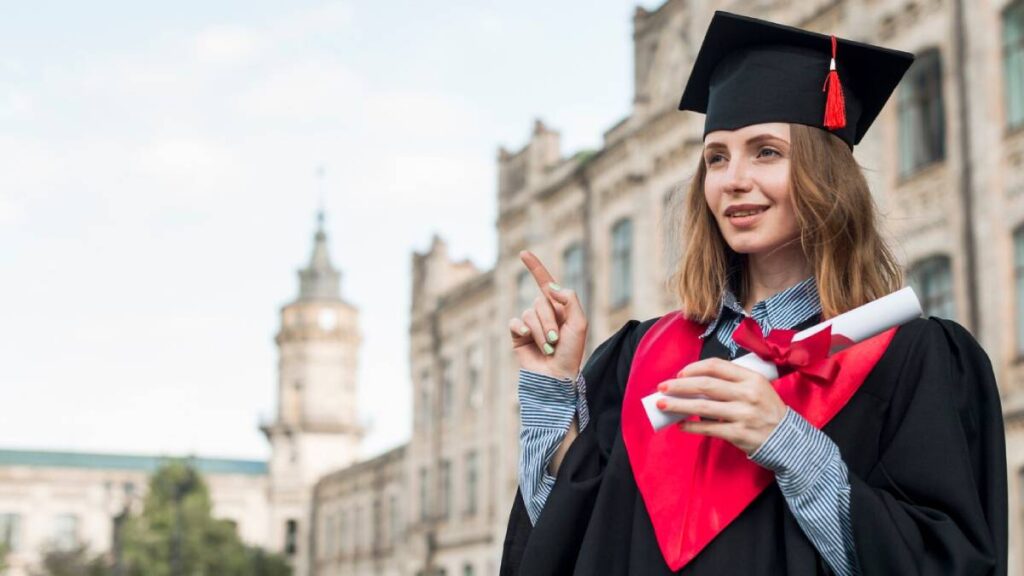 A woman in a graduation gown and cap points confidently, celebrating her academic achievement.