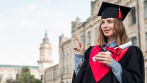 A woman in a graduation gown and cap points confidently, celebrating her academic achievement.