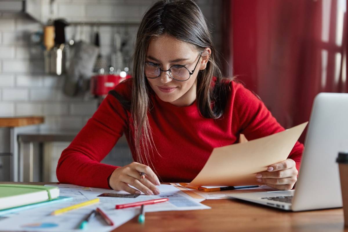 A woman wearing glasses is focused on completing paperwork at her desk.