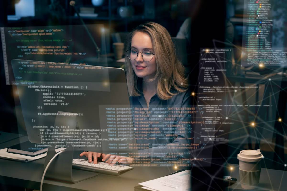 A woman focused on coding at her computer, with lines of code displayed on the screen in front of her. 