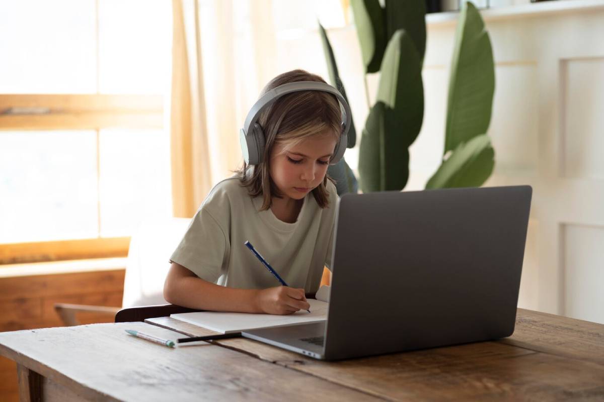 A young girl with headphones is focused on her laptop, engaged in her work or study. 