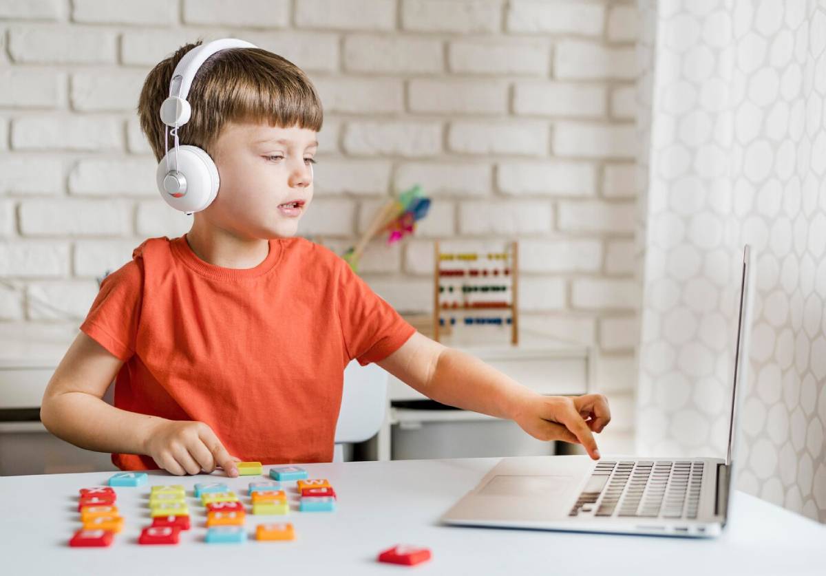  A young boy with headphones is focused on playing with a laptop, immersed in his digital activity. 