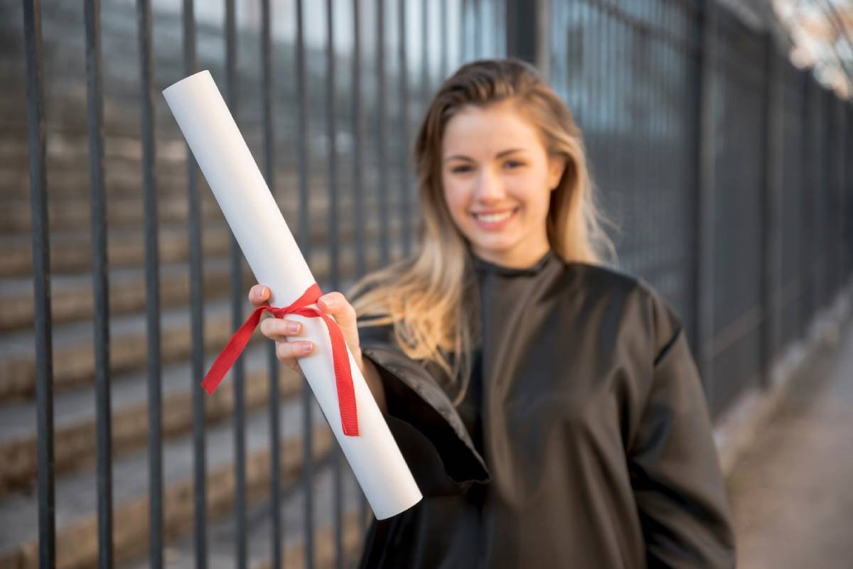 A woman in a graduation gown proudly holds her diploma, celebrating her academic achievement. 