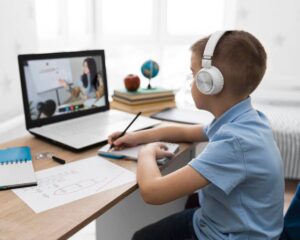 A boy with headphones sits at a desk, focused on his laptop while working or studying.