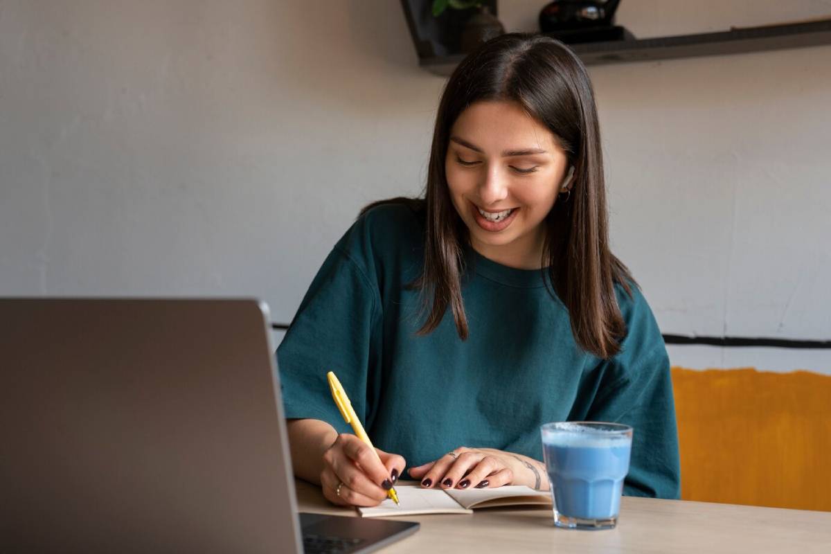woman smiles while writing in a notebook, showcasing a moment of creativity and focus.