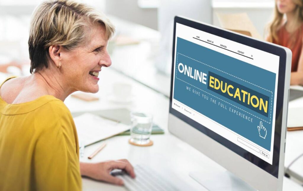 A woman in a yellow shirt sits at a desk using a computer displaying an Online Education website in a modern workspace.