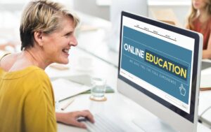 A woman in a yellow shirt sits at a desk using a computer displaying an Online Education website in a modern workspace.