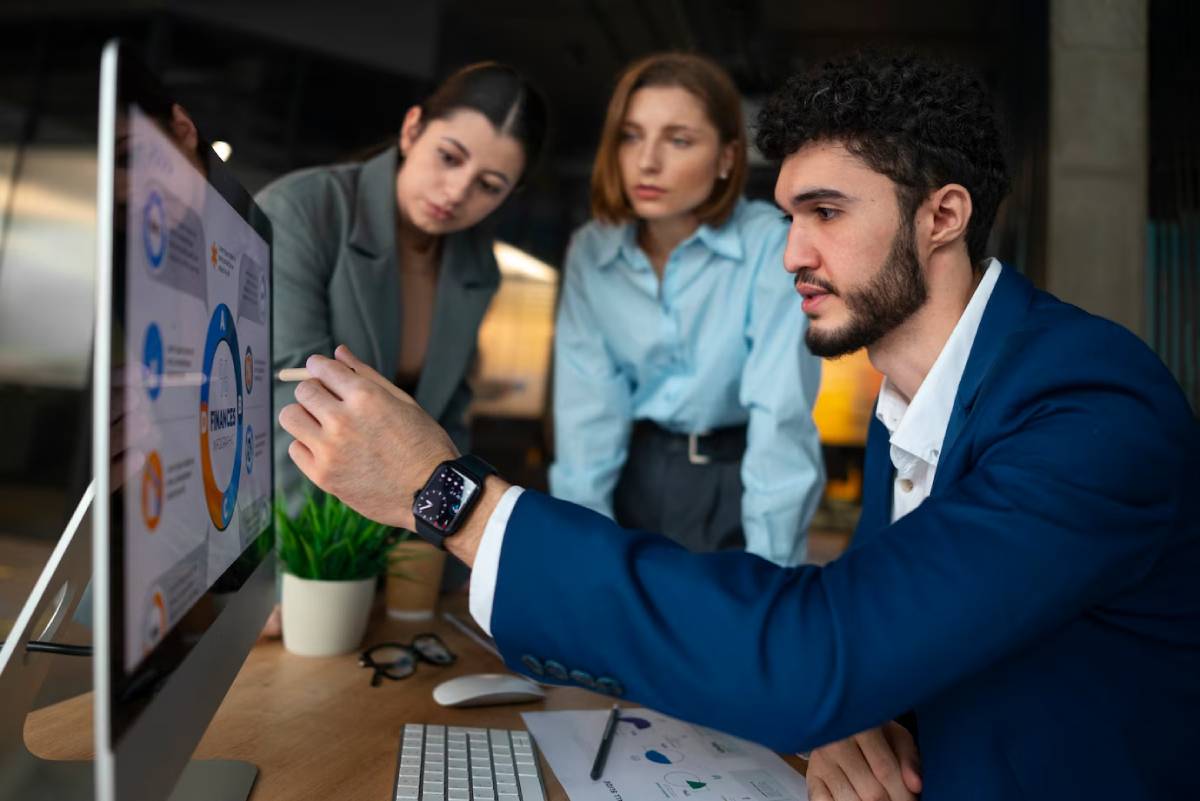 A group of business professionals collaborating while working on a computer in a modern office setting.