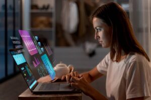 A person in a white shirt operates a laptop, with vibrant data visualizations displayed on the screen and a teapot nearby.