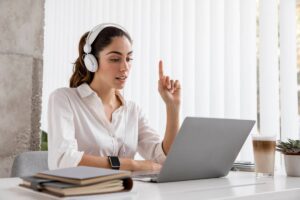A woman with headphones sits at a desk, focused on her laptop while working or studying.