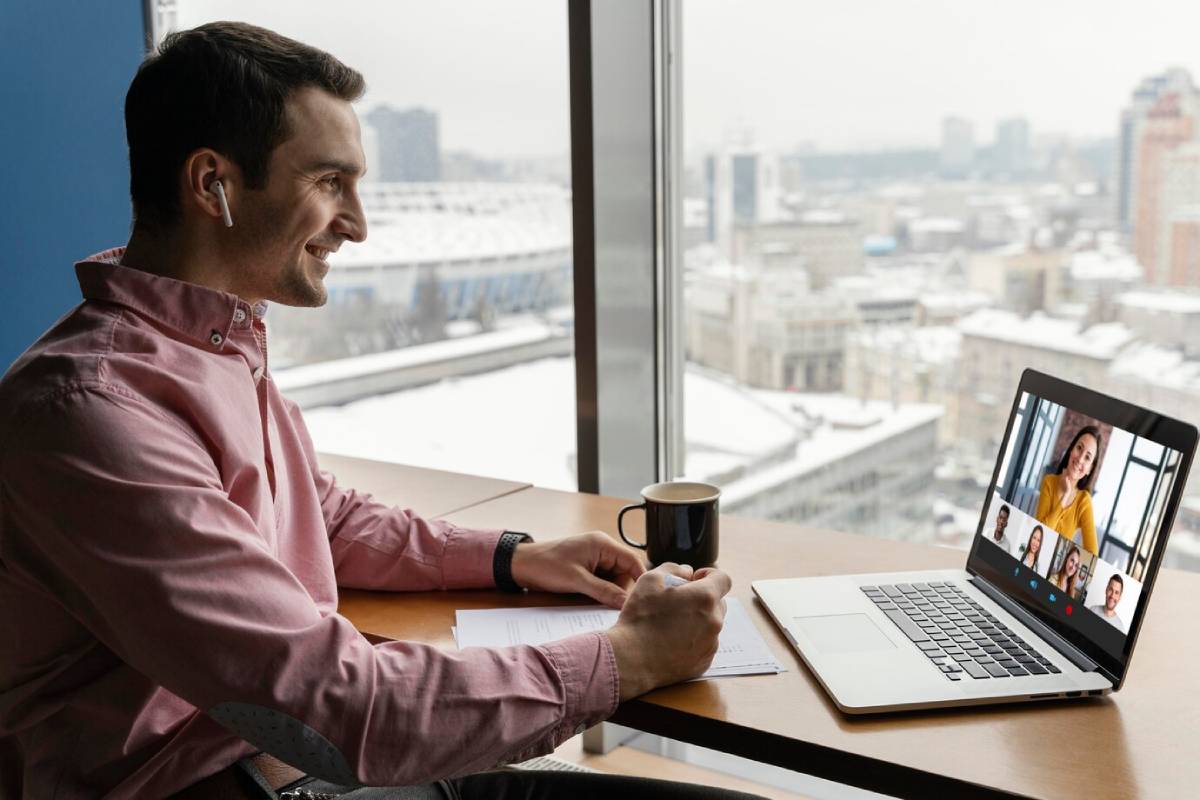 A man seated at a desk, working on a laptop with a camera positioned nearby.