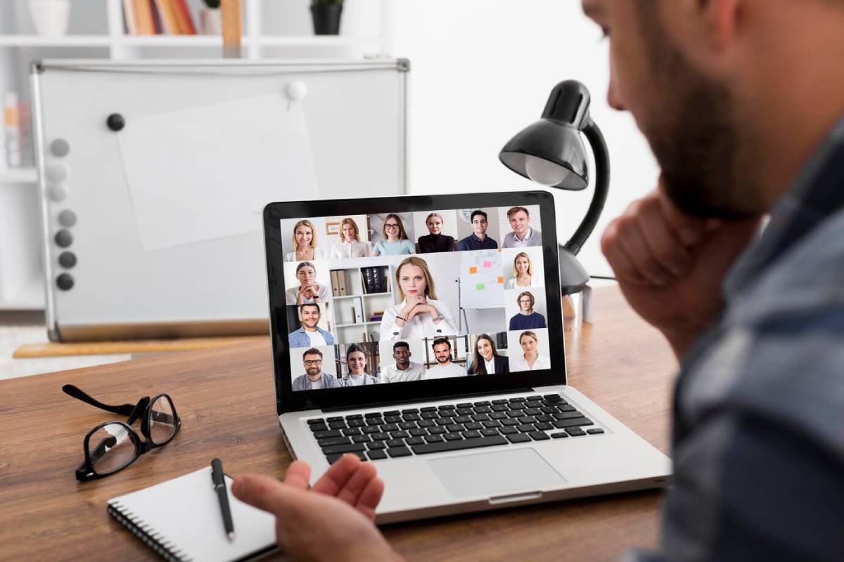 A man is engaged in a video conference while using a laptop at a desk.