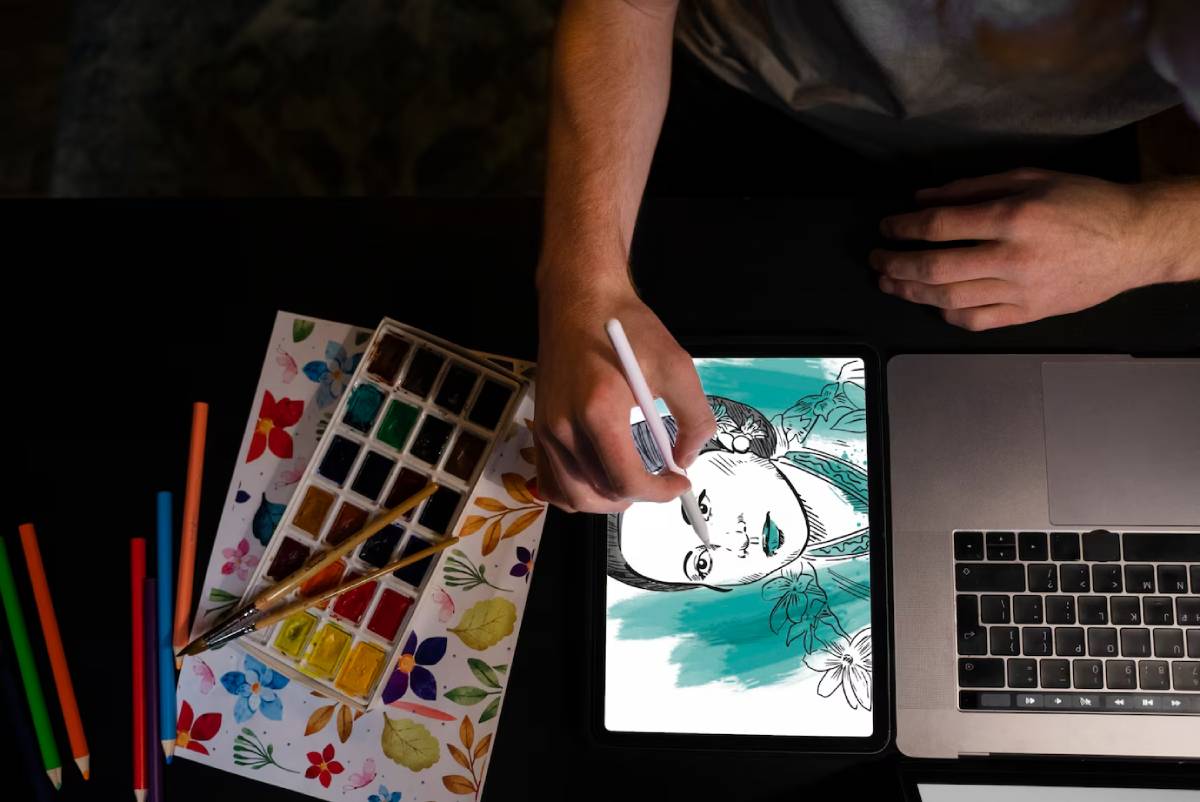 A person is drawing on a tablet while using a laptop, focused on their creative work.