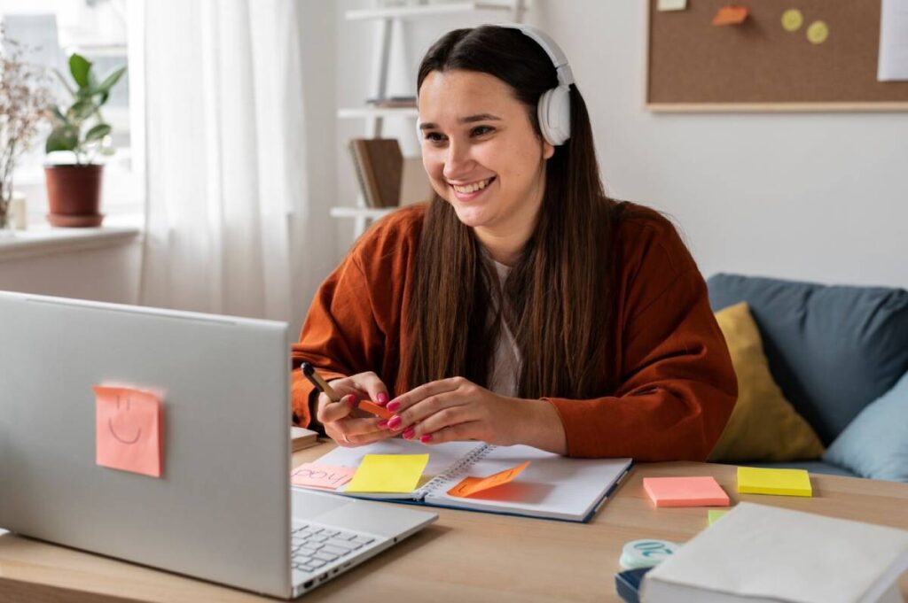 A woman sits at a desk with a laptop and headphones, focused on her work in a well-lit environment.
