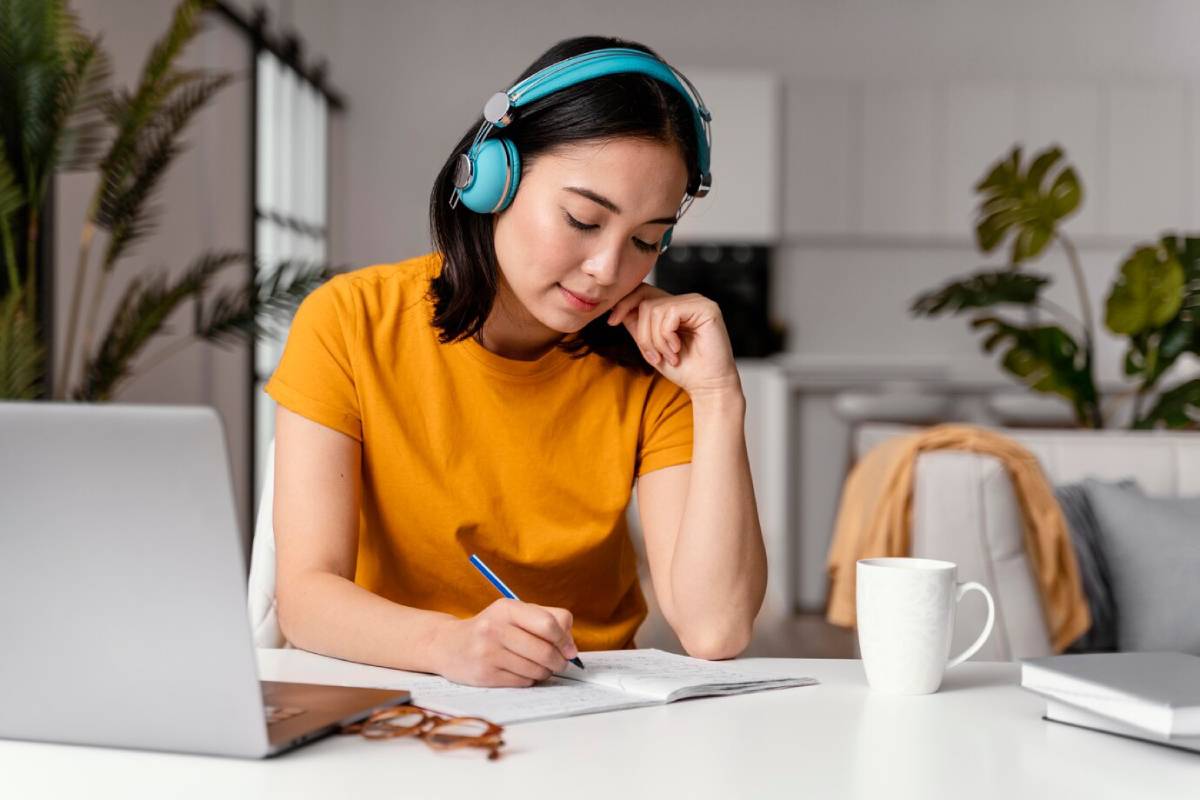 A woman with headphones is intently working on her laptop, immersed in her tasks.
