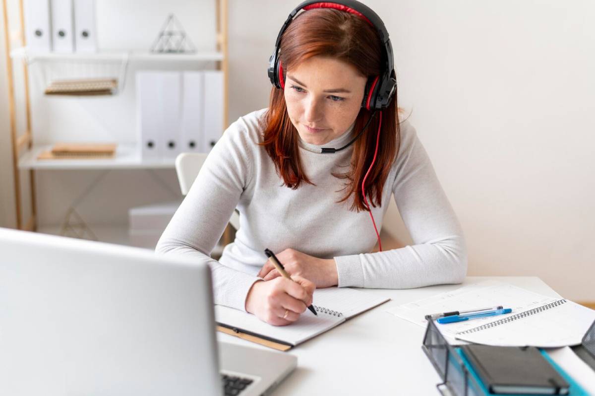 A woman wearing headphones is focused on her laptop, engaged in work.