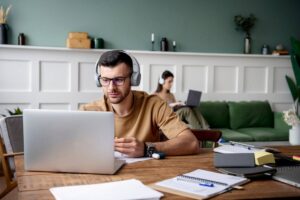 A man wearing headphones is focused on his laptop, engaged in work.