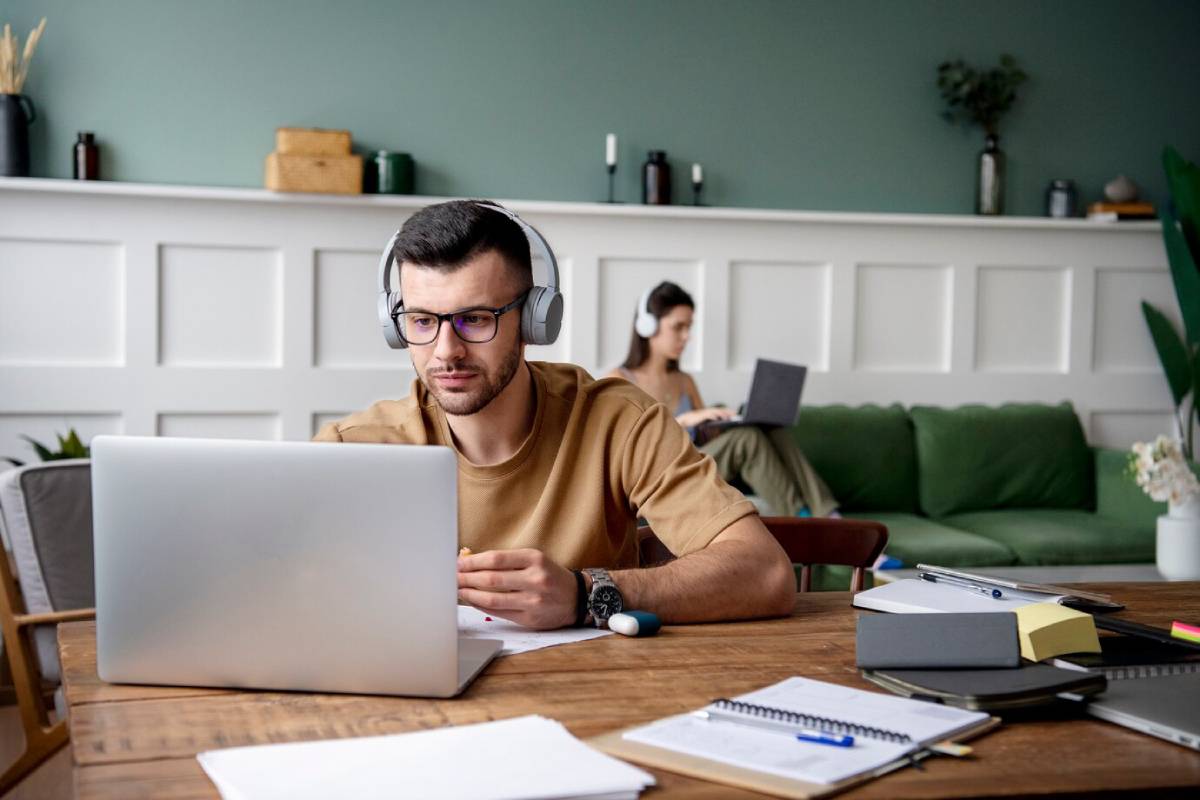 A man wearing headphones is focused on his laptop, engaged in work.
