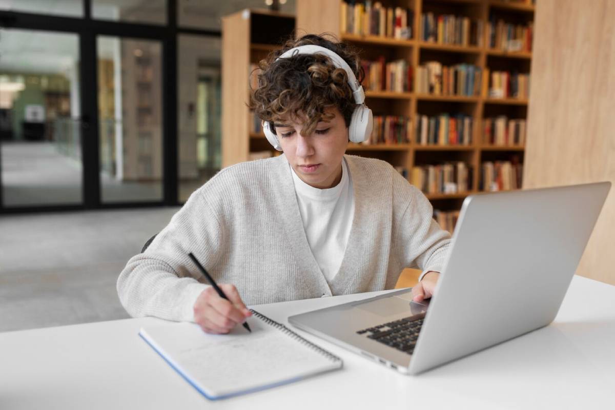 A young woman wearing headphones is focused on her laptop while working in a bright, modern workspace. 