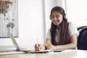 A girl wearing headphones is focused on her laptop while working on a project.