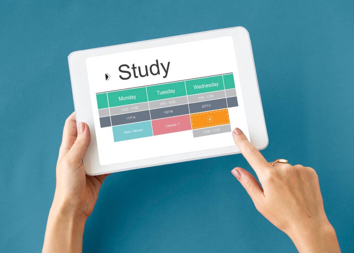 A person holding a tablet displaying a study schedule with times and classes for Monday, Tuesday, and Wednesday on a teal background. 
