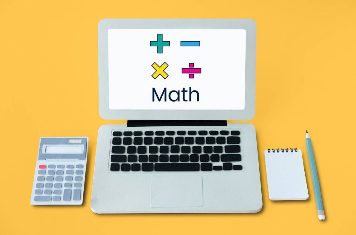 A laptop displaying math symbols (+, -, ×, ÷) alongside a calculator, notepad, and pencil, on a yellow background.