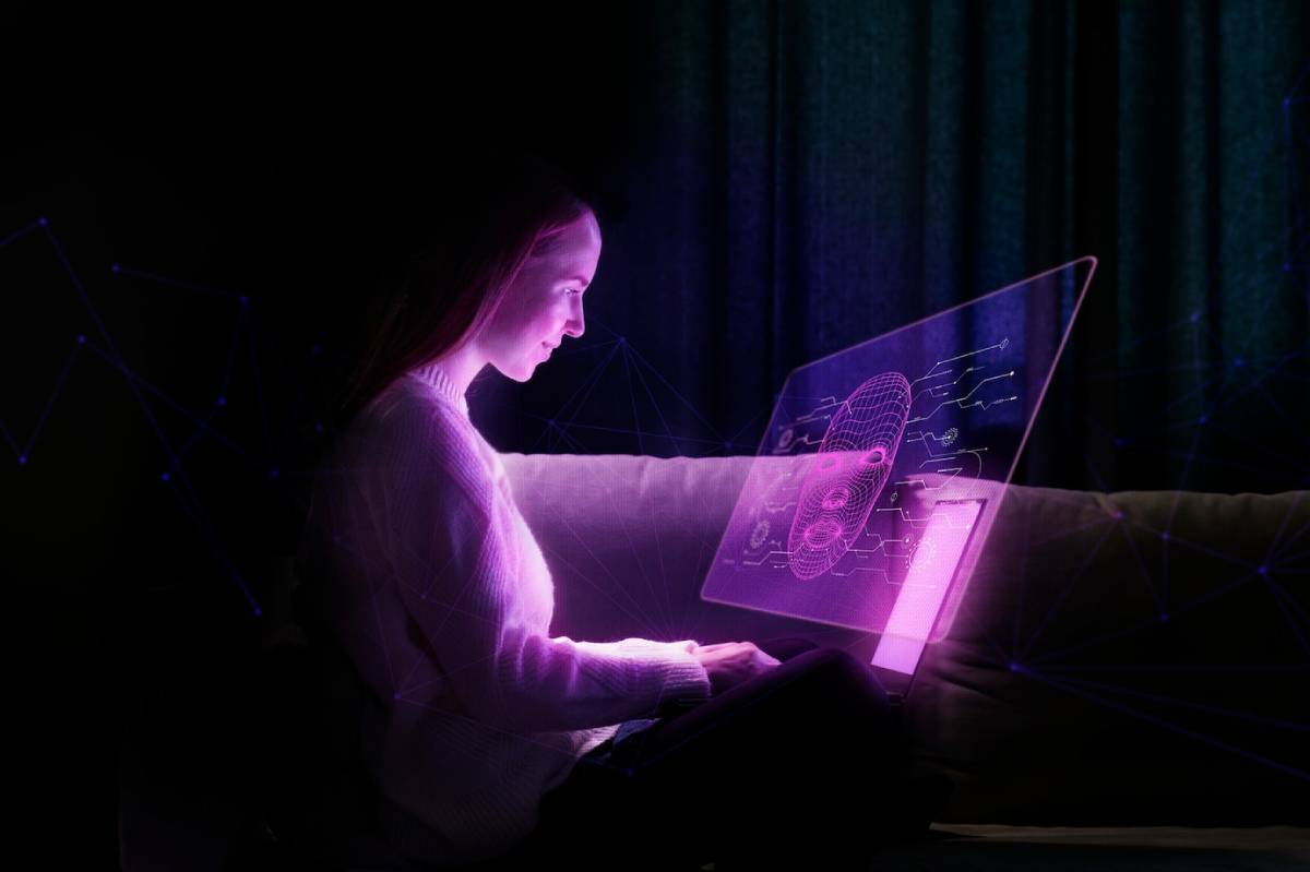 A person sits on a couch using a futuristic, transparent screen displaying digital graphics in shades of purple and pink. 