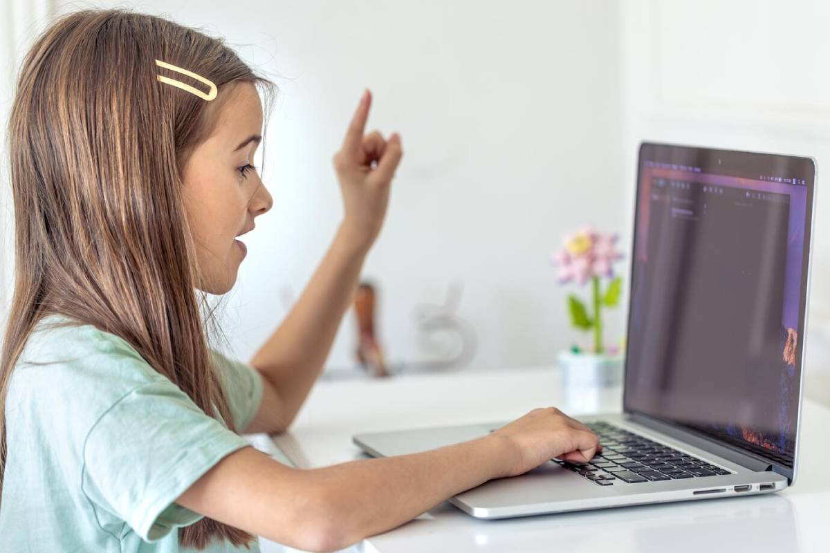 A girl with long brown hair sits at a desk, solving quizzes or exercise while using a laptop, with a potted flower nearby.