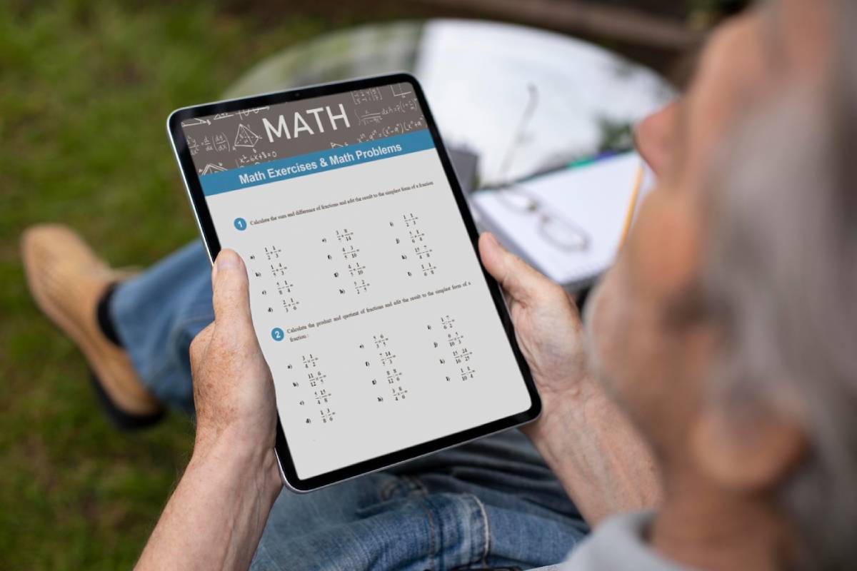 A person sitting outdoors holds a tablet displaying math exercises and problems, surrounded by grass.
